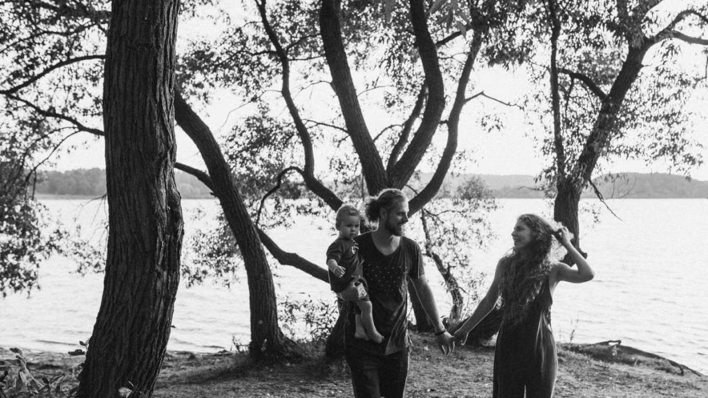 A joyful family strolls by the lakeside, surrounded by trees and nature.